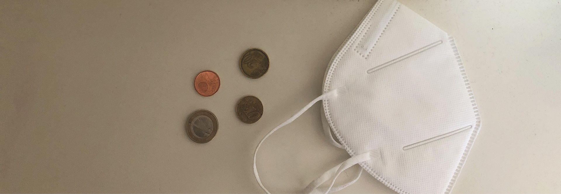Eine FFP2-Maske und Geldmünzen liegen auf einem Tisch. 