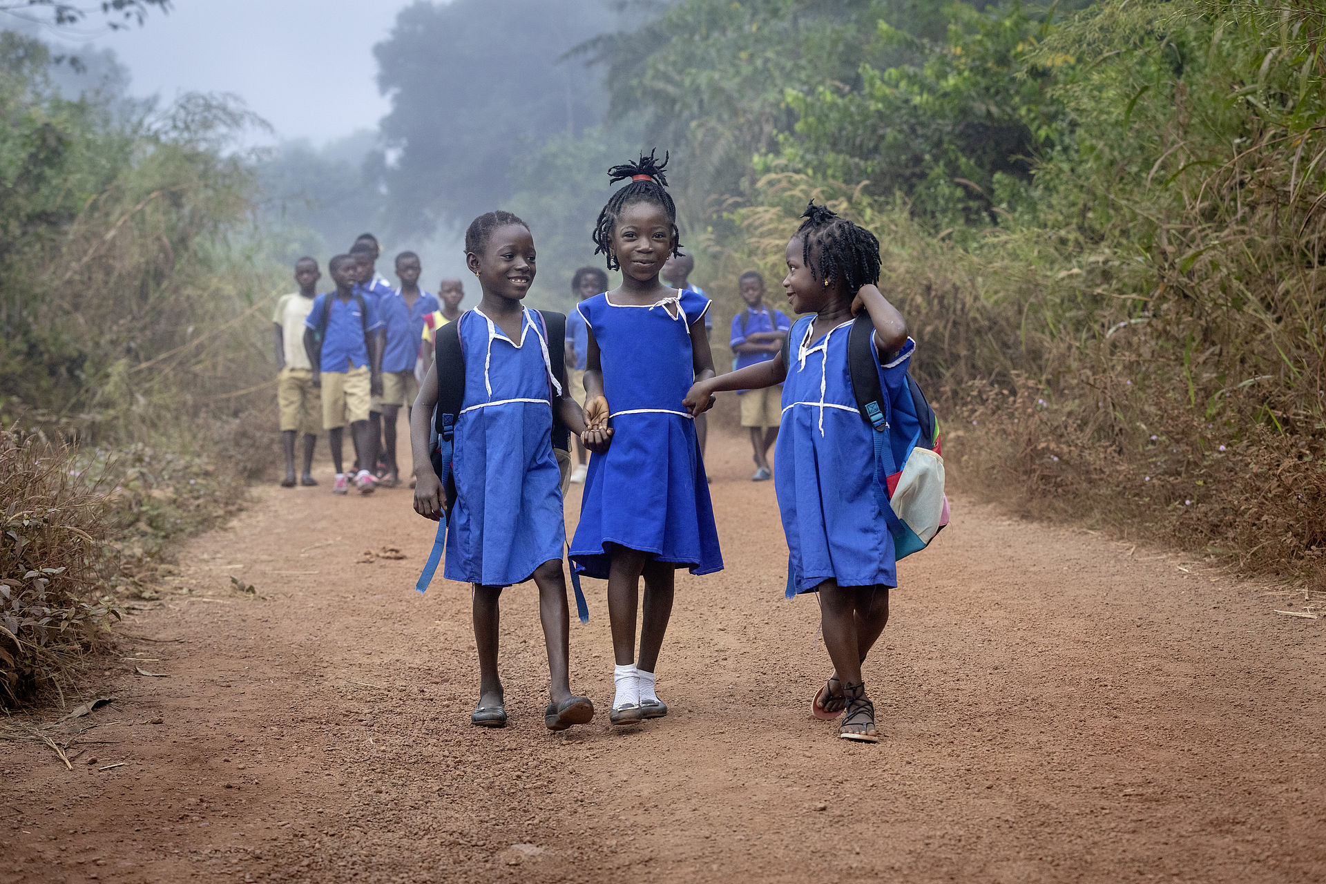 Drei Mädchen, alle in Schuluniform, sind auf dem Weg in die Dorfschule, die nahe dem Dorf Mamorka in  Sierra Leone liegt. 